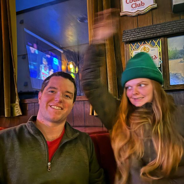 Lisa and Paul at a bar. Lisa's wildly waving her hands